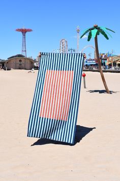 a blue and red striped towel sitting on top of a sandy beach next to a palm tree