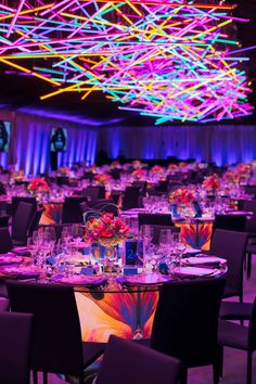 a room filled with lots of tables and chairs covered in purple cloths, lit by colorful lights