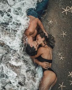 black and white photo of two people in bathing suits kissing on the beach with starfish