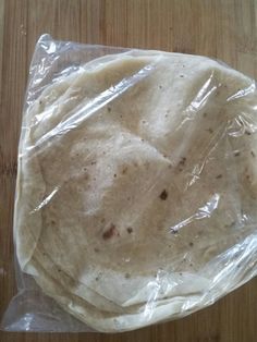 an uncooked tortilla wrapped in plastic on a wooden table