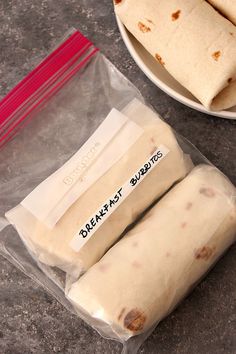 two burritos sitting on top of a counter next to a plate of food