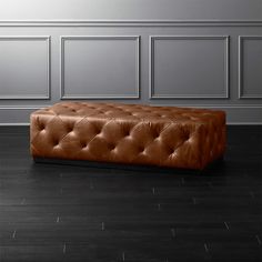 a brown leather bench sitting on top of a hard wood floor next to a gray wall