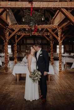 a bride and groom kissing in the middle of a room with lights strung from the ceiling