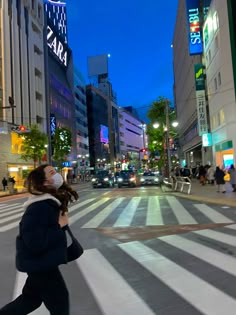 a woman wearing a face mask crosses the street in an urban area at night time