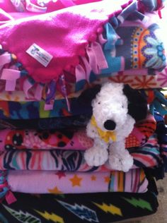 a pile of colorful blankets with a stuffed dog sitting on top of one in the middle