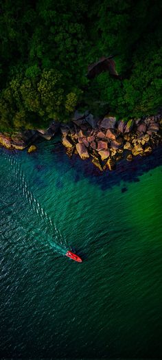 an aerial view of a boat in the water near some rocks and green trees at night