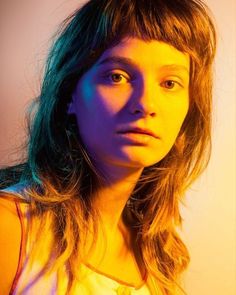 a woman with long hair is looking at the camera while wearing a white shirt and blue light