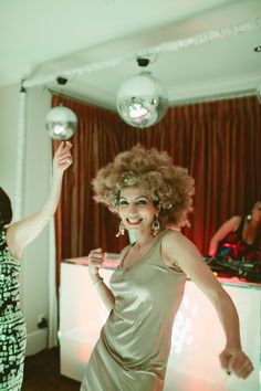 a woman with curly hair is dancing on the dance floor in front of disco ball lights