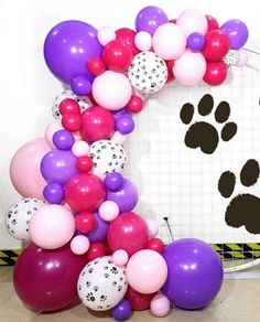 the balloon arch is decorated with paw prints and pink, purple, and white balloons