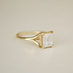 a yellow gold ring with an emerald cut diamond in the center, sitting on a white surface