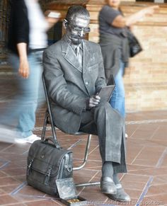 a statue of a man sitting on top of a chair holding a briefcase and looking at his cell phone