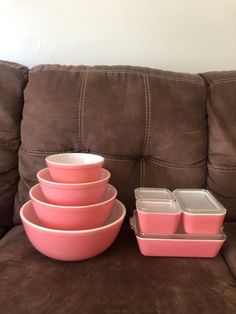 pink dishes are stacked on top of each other in front of a brown coach cushion