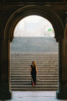 a woman is walking down some steps in an arch with stairs leading up to her