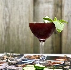 a close up of a wine glass on a table with cucumbers around it