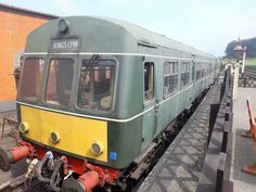 a green and yellow train sitting on the tracks next to a brick building with windows