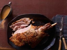 a roasting pan filled with meat on top of a wooden table next to utensils