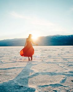 a woman in an orange dress is walking through the snow with her surfboard on