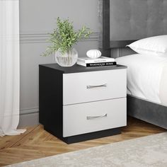 a nightstand with two drawers and a potted plant next to it on a bed