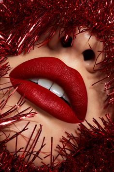 a woman's face with red lipstick and tinsel on her body, in front of christmas tinsel