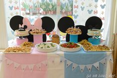 a table topped with lots of food next to a mickey mouse cake and cupcakes