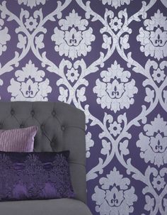 a bed with purple and white pillows on top of it next to a wallpaper