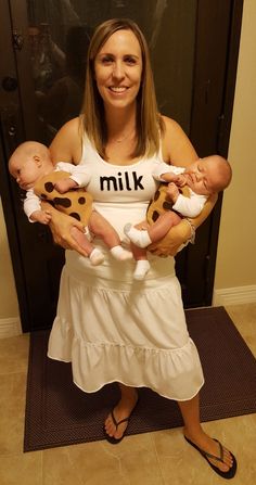 a woman is holding two babys in her arms and smiling at the camera while wearing a milk t - shirt