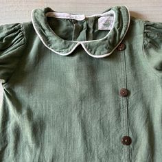 a green shirt with buttons on the collar is laying on a white surface and there is no image to describe