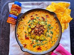 a skillet filled with cheese and olives next to chips