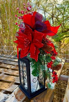 a lantern with poinsettis and pine cones is sitting on a wooden table