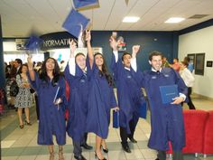 four students in blue graduation gowns holding up their caps and diplomas while posing for the camera