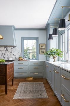 a kitchen with blue cabinets and marble counter tops, wood floors, gold accents and hanging lights