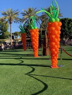 three carrot shaped balloons in the shape of trees on green grass with palm trees behind them