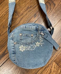 an old jean purse with embroidered flowers on the front and side pockets, sitting on a wooden floor