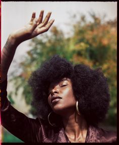 a woman with an afro is holding her hand up in the air and looking upward