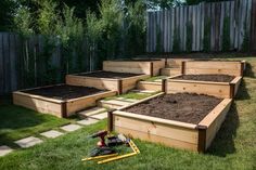 several wooden raised garden beds with gardening tools on the ground in front of them,