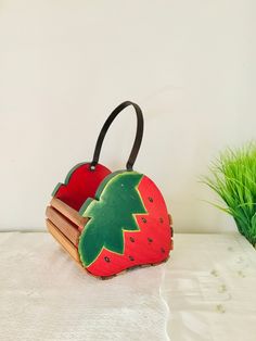 a strawberry shaped purse sitting on top of a table next to a potted plant