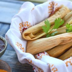 several tamales with cilantro and parsley sit in a bowl next to dipping sauce