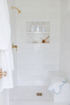 a bathroom with white tile and gold faucet shower head, soap dispenser on the wall