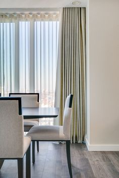 a dining room table and chairs in front of a window with drapes on it