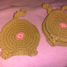 two crocheted hats sitting on top of a pink blanket