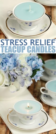 blue and white teacups with flowers in them on a wooden table next to a candle