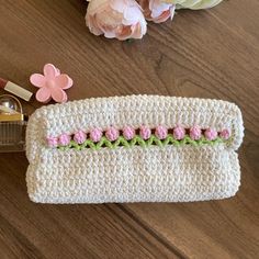 a crocheted purse sitting on top of a wooden table next to pink flowers