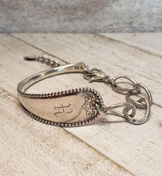 a silver bracelet with an anchor and cross on the clasp, sitting on a wooden surface