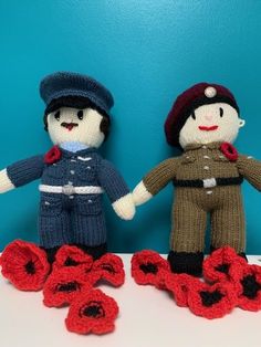 two crocheted dolls are standing next to each other on a table with red flowers