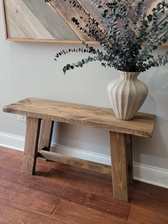 a wooden bench with a vase on top of it next to a painting and wood flooring