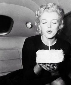 a black and white photo of a woman blowing out a candle on a birthday cake