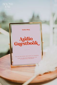 an audio guest book sitting on top of a wooden table next to a white feather