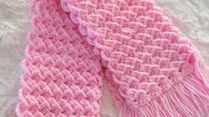 a pink crocheted scarf laying on top of a white blanket