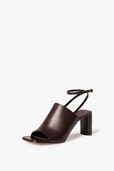 The Alina Sandal is one of this season's most versatile shoe shapes, thanks to a wearable 75mm heel that pairs well with both tailoring and dresses. It features a squared toe shape built on a oval, sculptural heel ‚Äì¬†new to VB Footwear ‚Äì and a minimalist cross-over band with waxed raw edges in natural tumbled calf leather for a laidback, 90s feel. An adjustable ankle strap, hand stitched to the cross-over band, offers an effortless finish. Victoria Beckham Alina Sandal in Dark Brown  - Size Shoe Shapes, Toes Designs, Leather Heels Sandals, Heeled Sandal, And Dresses, Leather Band, Victoria Beckham, Dark Black, Hand Stitched