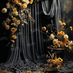 an arrangement of flowers on a table in front of a black drapeed curtain